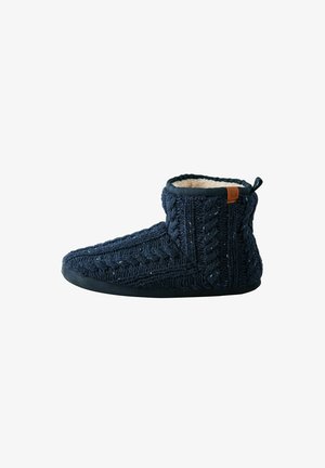 Marineblau gestrickter Hausschuh mit einem Kabelmuster, weichem Fleece-Futter und einer schwarzen Gummisohle. Verfügt über einen braunen Ledereinsatz auf der Rückseite.