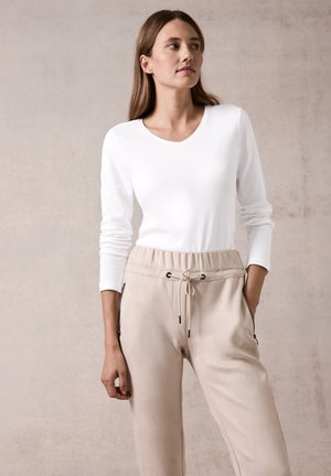 Maglietta bianca a maniche lunghe con scollatura a V abbinata a pantaloni beige con coulisse, dotati di tasche laterali con zip e una vestibilità comoda. Texture liscia complessivamente.