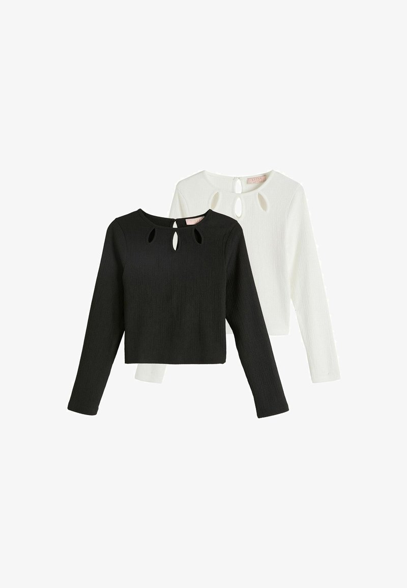 Svart och vit långärmad croppad topp med texturerad tyg, med tre nyckelhålsutskärningar vid halslinningen och en rund krage.