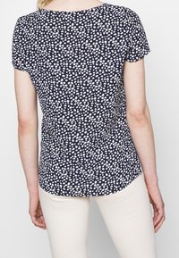 Námořnický top s krátkým rukávem s bílým tečkovaným vzorem, kulatým výstřihem a postranními rozparky pro snadný pohyb. Lehká látka s hladkým povrchem.