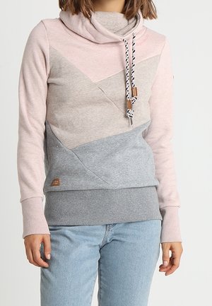 Frau trägt einen Hoodie im Farbblock-Design in Pink, Beige und Grau mit Kordelzug am Kragen und hellblauen Jeans.