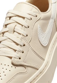 Beige kožené sneakersy s texturovaným povrchem, bílé tkaničky a bílým logem swoosh. Obsahuje perforace na špičce a prošívané detaily.