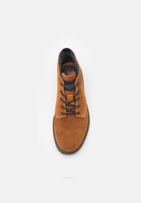 Zapato de ante marrón hasta el tobillo con cordones azul marino, puntera redonda y costuras en contraste. Interior forrado suave, suela de goma plana.