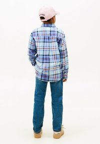 Ruitjeshemd in blauw, wit en rood, gecombineerd met blauwe spijkerbroeken en lichtgekleurde sneakers. Een roze pet wordt achterstevoren gedragen.