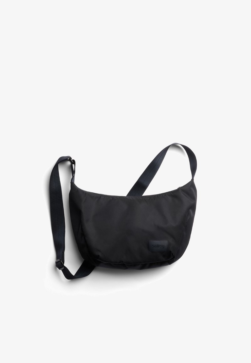 Sac d'épaule en nylon noir avec une forme incurvée, une sangle réglable et un patch logo subtil. Caractérisé par une texture lisse et une fermeture éclair.