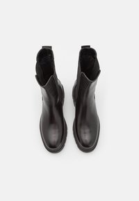 Bottes noires en cuir à la cheville avec une finition lisse, des panneaux élastiques sur les côtés et une semelle en caoutchouc noir robuste. Boucles à l'arrière pour un enfilage facile.