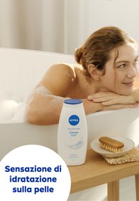 Bottiglia di schiuma da bagno NIVEA Creme Soft, bianca con tappo blu, mostrata accanto a un piatto di legno con una spazzola con setole naturali su una superficie di legno.