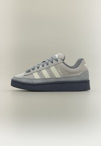 Γκρι σουέτ αθλητικό παπούτσι με τρεις λευκές ρίγες, υφασμένο επάνω μέρος, στρογγυλή μυτερή άκρη και επίπεδη μαύρη λαστιχένια σόλα. Διαθέτει διακριτικό λογότυπο στο πλάι.