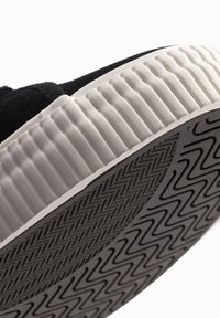 Sneaker nera in tela con suola in gomma bianca testurizzata e motivo a zigzag. Il lato presenta dettagli in tessuto e cuciture nere.