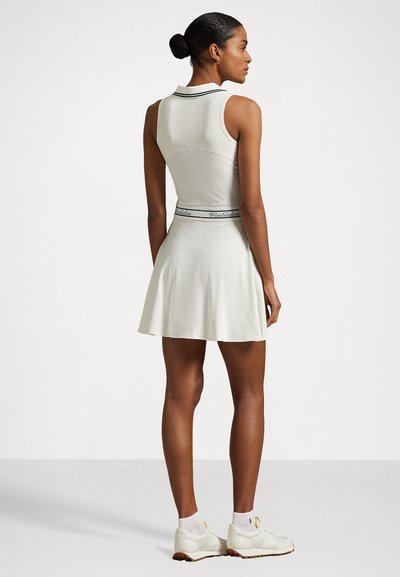 Weißes Sportkleid mit tailliertem Oberteil und schwingendem Rock, ausgestattet mit einem oberen Teil aus Mesh, einem Kragen mit schwarzem Saum und einem Taillenband mit Wimbledon-Logo.