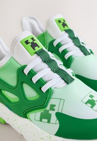 Baskets vertes et blanches avec des visages de Creeper pixélisés, des lacets blancs et des accents verts sur une semelle tachetée.
