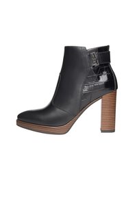 Bota de tobillo de cuero negro con punta afilada, panel de cuero sintético texturizado y tacón grueso de madera a rayas. Presenta un detalle de hebilla lateral.