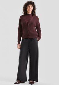 Bordowy sweter na guziki z dekoltem w serek, zestawiony z szerokimi czarnymi spodniami, charakteryzujący się gładką fakturą i luźnym krojem.