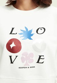 Sudadera blanca con la palabra "AMOR" en letras negras y diseños gráficos coloridos: flor azul, círculo rojo con estrella, forma rosa, corazón blanco.