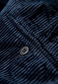 Marineblauwe corduroy stof met verticale ribbels en een zwart viergaatjesknopdetail, dat de textuur en het patroon benadrukt.