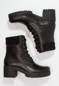 Bottines en cuir noir avec talon épais, bout rond et laçage à l'avant. Présentent un accent en daim en haut et une semelle en caoutchouc texturée.