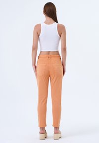 Pantalon orange pour femmes, coupe ajustée, taille mi-haute, avec deux poches arrière et une ceinture cousue. Porté avec un débardeur blanc ajusté.