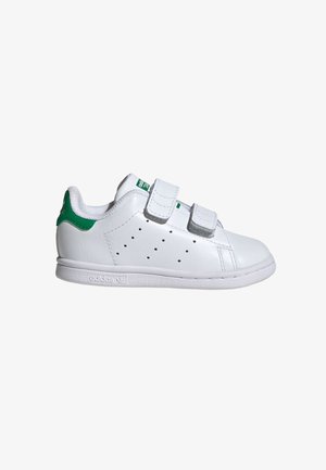 Biała tenisówka Adidas z zielonym uchwytem na pięcie, dwoma paskami na rzep oraz perforowanymi otworami po bokach na jednolitym białym tle.