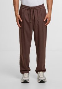 Bruine, lichte, taps toelopende broek met een elastische tailleband en koord. De stof heeft een gladde textuur, geschikt voor casual draagstijl.