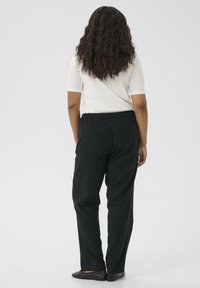 Pantalons noirs avec ceinture élastique, poches latérales et coupe droite, associés à un haut léger à manches courtes. Texture lisse.