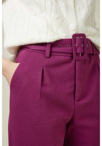Pantalon violet sur mesure avec une large ceinture dotée d'une boucle rectangulaire, poches latérales et plis sur le devant ; fabriqué à partir d'un tissu doux et texturé.
