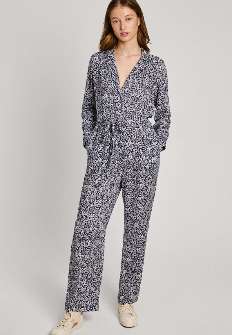 Floralni leotard v temno modri barvi z dolgimi rokavi, V-izrezom, zategnjenim pasom in žepi, v kombinaciji s svetlobarvnimi supergami.