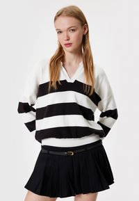 Sweter w czarno-białe paski z dekoltem w serek i luźnym krojem, w połączeniu z czarną spódnicą plisowaną z cienkim paskiem.