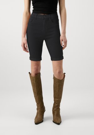 Shorts de mezclilla negra con un ajuste ceñido, con los puños doblados, combinados con botas altas de cuero marrón que presentan costuras decorativas y una punta afilada.