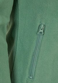 Section d'une veste en polaire verte avec une poche zippée. Le tissu a une texture douce, et la fermeture éclair est métallique avec une boucle pour une prise facile.