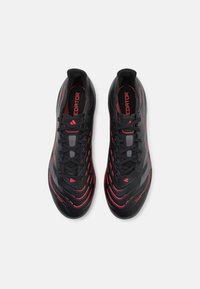 Black athletic shoes with red accents, sleek design, textured upper, prominent lacing, and "PREDATOR" branding on the tongue.