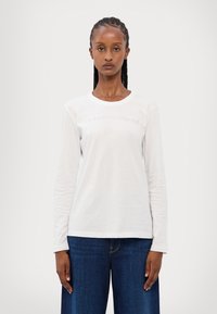 Camicia bianca a maniche lunghe con collo rotondo, caratterizzata da testo in rilievo "Armani Exchange" sul petto. Materiale in cotone morbido.