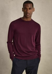 Burgundy långärmad tröja med rund hals, tillverkad av ett slätt tyg, med en figursydd silhuett och ribbade ärmslut och nederkant.