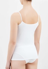 Canotta bianca in cotone con spalline sottili, design aderente e texture morbida, abbinata a biancheria intima bianca coordinata, vista dal retro.