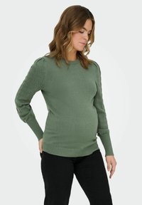 Zeleni pleteni pulover s okroglim izrezom, ki ima rebraste manšete in teksturiran vzorec na rokavih. Slim fit zasnova.