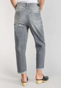 Harmaat suoralahkeiset farkut, joissa on kaksi takataskua, käännetyt lahkeet ja hienovaraiset kulutusjäljet. Yhdistetty mustiin puukenkään.