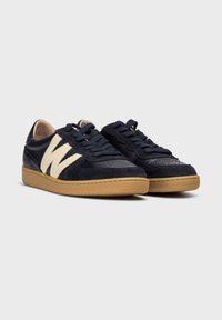 Zapatillas de ante y cuero en azul marino con acentos en crema, paneles texturizados, puntera redonda y suela de goma. Cuenta con cordones planos y detalle de logo.