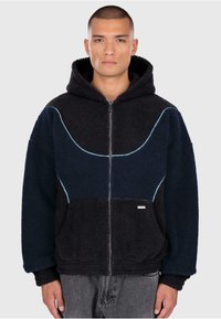 Hooded zip-jacka i marinblå och mörkblå fleece med kontrasterande ljusblå sömmar och framfickor. Mjuk textur, avslappnad passform.