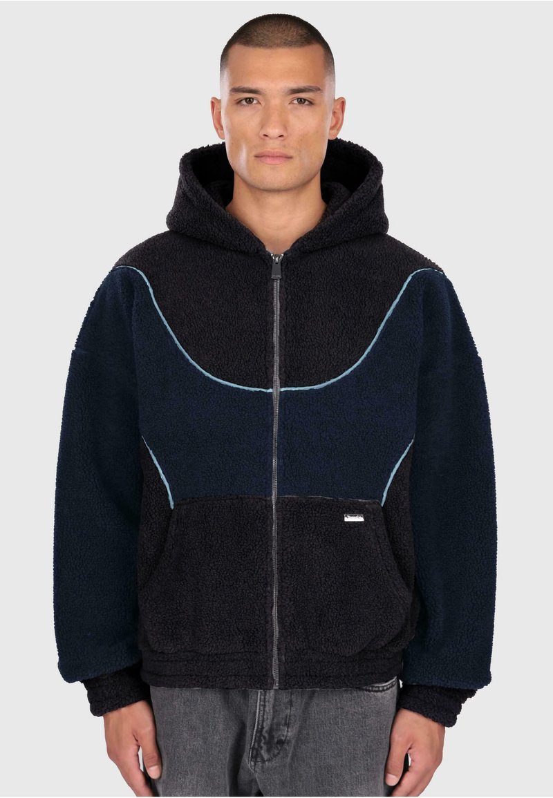Hooded zip-jacka i marinblå och mörkblå fleece med kontrasterande ljusblå sömmar och framfickor. Mjuk textur, avslappnad passform.