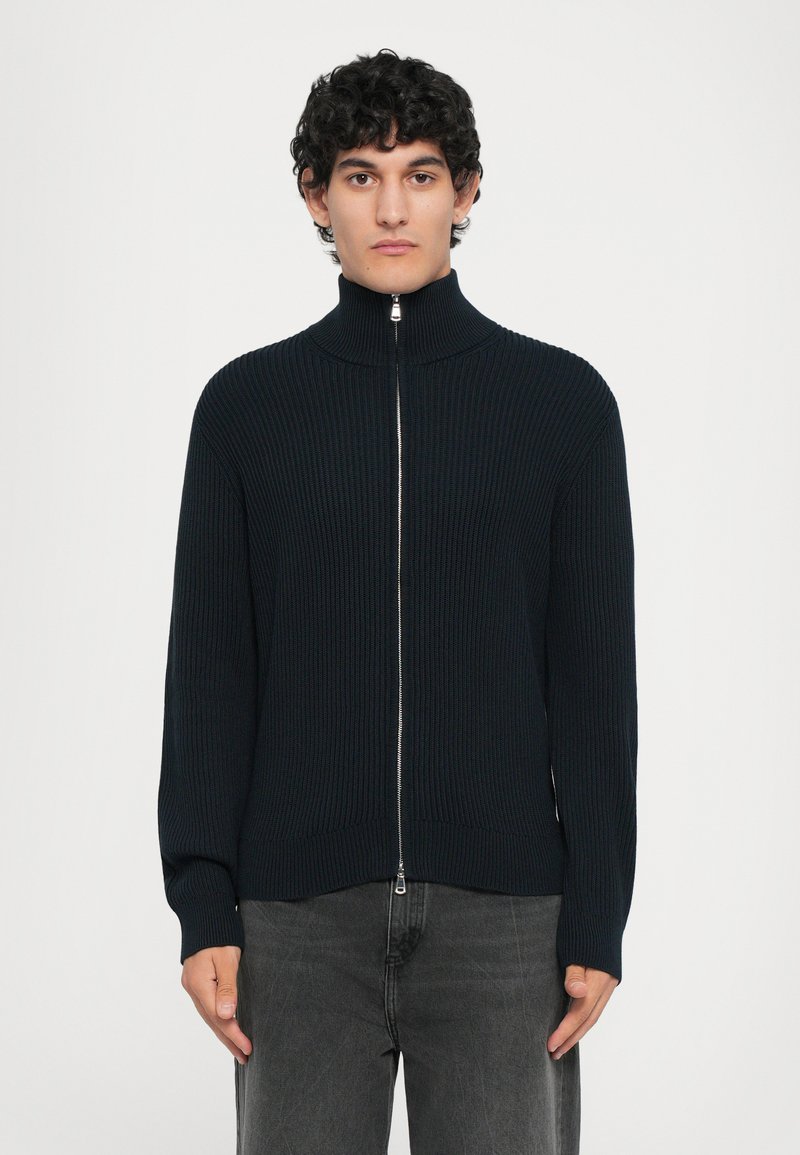 Mörk marinblå ribbad stickad zip-sweater med hög krage och silverfärgad dragkedja, med långa ärmar och en avslappnad passform.