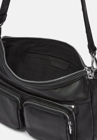 Borsa in pelle nera con cerniere argentate. L'interno è foderato in tessuto nero. Presenta numerose tasche con cerniera e una tracolla.
