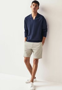 Suéter navy con cuello en V, pantalones cortos gris claro y zapatillas blancas. El conjunto presenta un ajuste relajado y textura suave.