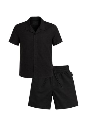 Camicia nera a maniche corte con bottoni e colletto a lancia, abbinata a pantaloncini neri con vita elastica e coulisse.