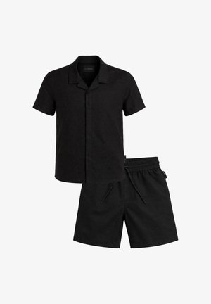 Camicia nera a maniche corte con bottoni e colletto a lancia, abbinata a pantaloncini neri con vita elastica e coulisse.