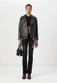 Giacca da moto in pelle nera con zip argentate, top nero corto, jeans neri a campana e stivaletti in suede marrone. Piccola borsa con dettaglio.