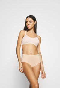Nude sömlös bh och högmidjade trosor i stretchigt material. Båda har släta ytor och minimal sömnad för komfort och diskret användning.