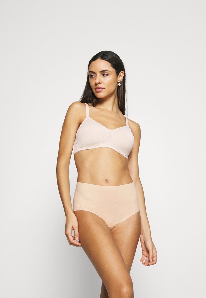 Nude sömlös bh och högmidjade trosor i stretchigt material. Båda har släta ytor och minimal sömnad för komfort och diskret användning.
