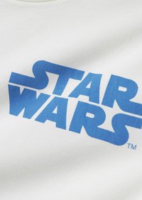 Vit bomull t-shirt med en framtr ädande blå "STAR WARS" logotyp i en djärv, retro stil. Slät textur utan ytterligare mönster eller detaljer.