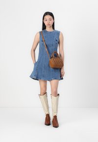 Denim A-lijn jurk met een mouwloos ontwerp. Bruine gestructureerde handtas en kniehoge laarzen met crèmekleurige accenten. Eenvoudige en functionele styling.