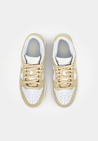 Biele a béžové tenisky Nike s perforovanou textúrou, štruktúrovanými materiálmi a plochými šnúrami, so štítkom na jazyku a na boku.