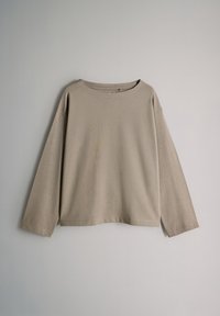 Camisa beige de manga larga con un corte holgado, cuello redondo y mangas puñadas. Textura suave y diseño minimalista.